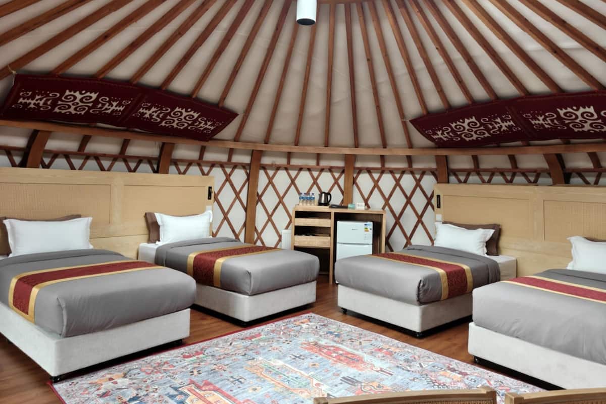A yurt-style room with four beds, a small desk, and a patterned rug.