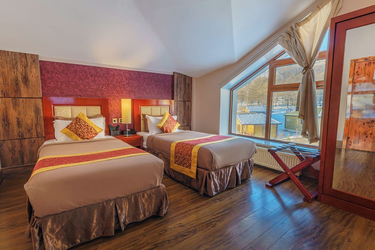 A hotel room with two beds, a large window with a view of the outside, and wooden flooring.