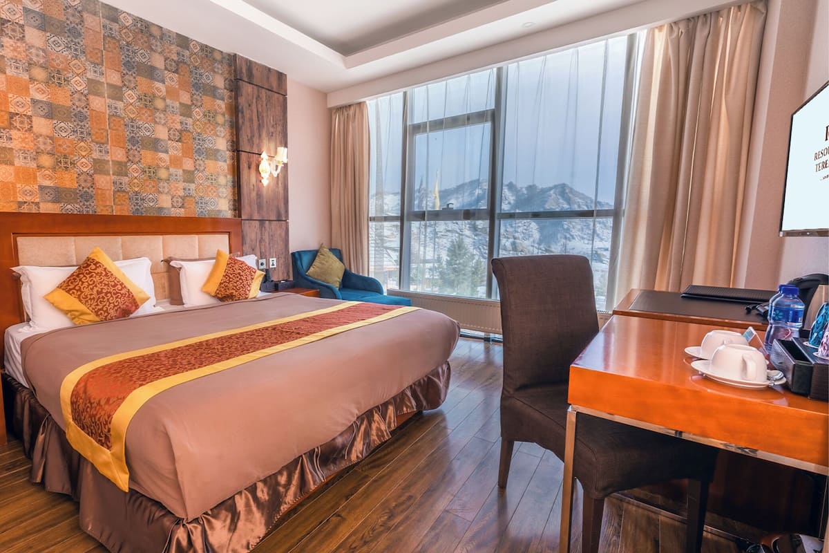 A hotel room with a large bed, a desk, and a view of a snowy landscape through the window.