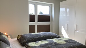 Ein Schlafzimmer mit einem Bett, zwei Nachttischen, einem Kleiderschrank und einem Fenster mit Jalousien.