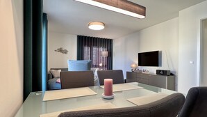 Ein modernes Hotelzimmer mit einem Glastisch, zwei Sofas, einem Fernseher und einem Flachbildfernseher auf einem Schrank.