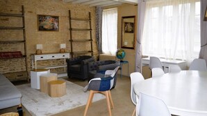 Ein gemütliches Wohnzimmer mit einer Couch, einem Couchtisch und einem Esstisch mit Stühlen. Auf einem kleinen Tisch steht ein Globus, und die Wände sind mit Kunstwerken geschmückt.