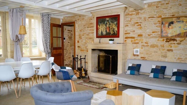 Ein gemütliches Wohnzimmer mit Steinwand, Kamin, einer Couch mit blauen Kissen und einem Essbereich mit weißen Stühlen.
