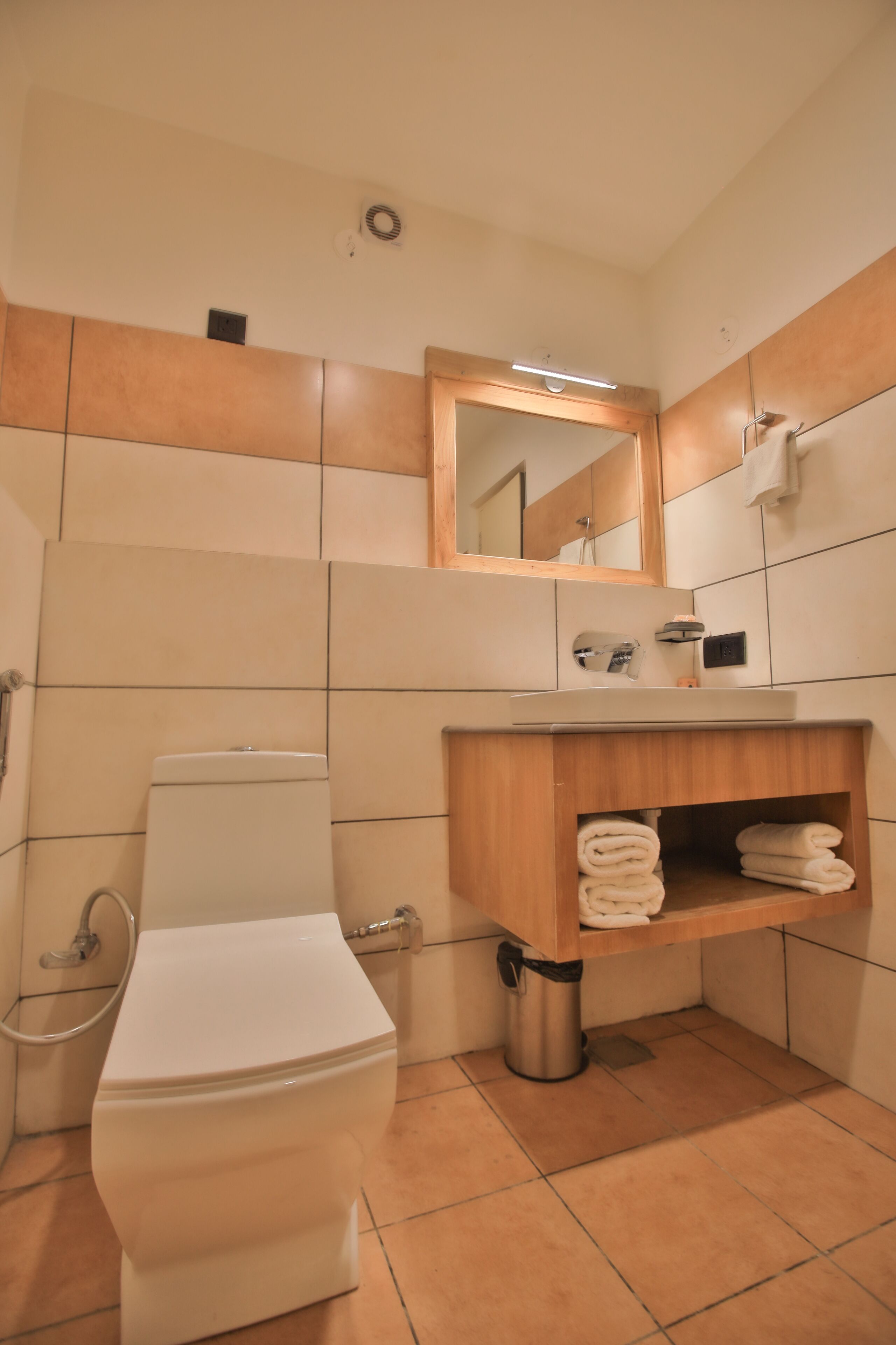 A bathroom with a toilet, sink, mirror, and towel storage.