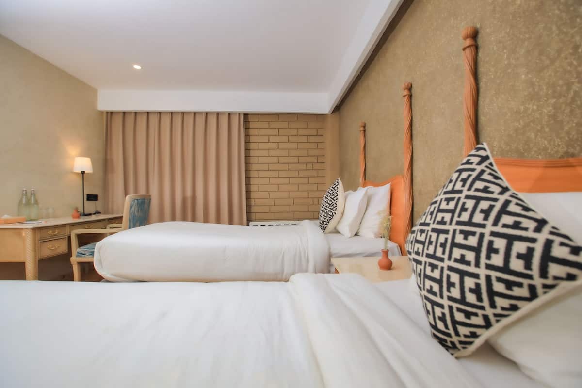 Ein Hotelzimmer mit zwei Betten, einem Schreibtisch, einem Stuhl, einer Lampe und einer Ziegelwand.