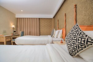 A hotel room with two beds, a desk, a chair, a lamp, and a brick wall.