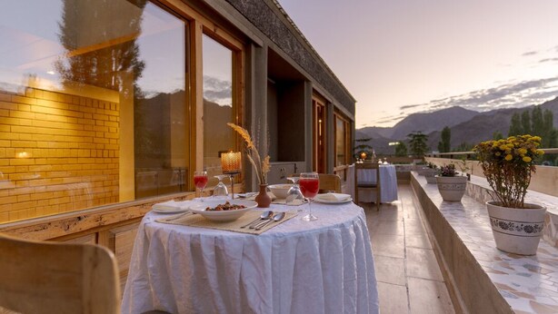 An outdoor dining area with a table set for two, overlooking a mountainous landscape. - The Pal (Leh)