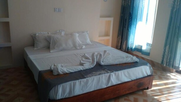Una cama con ropa de cama blanca y cabecera de madera, una mesita de noche y una ventana con cortinas.