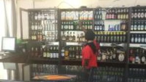 Zona de bar con estanterías llenas de botellas, una barra y una persona con camisa roja.