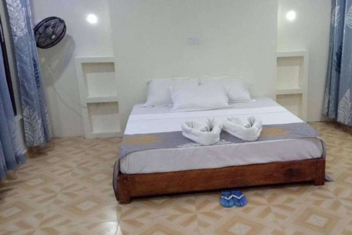 A neatly made bed with white linens and towels, a wooden headboard, and a patterned floor.