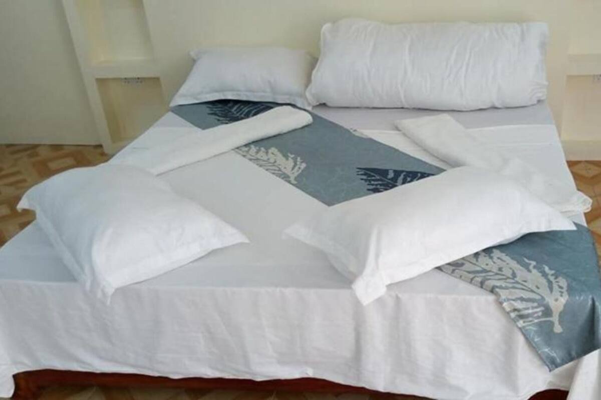 A bed with white and blue bedding, a patterned throw, and a wooden floor with a geometric pattern.