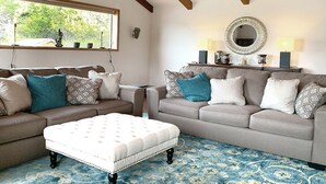 A living room with two sofas, a white ottoman, a large mirror, and a ceiling with exposed beams and hanging lights. - Luxurious Getaway on the Lake with hot tub, pool table, boat dock, covered porch (Langlois)