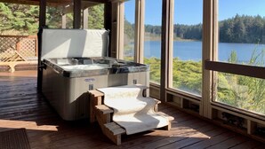 A hot tub on a wooden deck with a view of a lake and forest. - Luxurious Getaway on the Lake with hot tub, pool table, boat dock, covered porch (Langlois)
