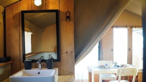 A wooden cabin interior with a white sink, a large mirror, and a dining area with a table and chairs.