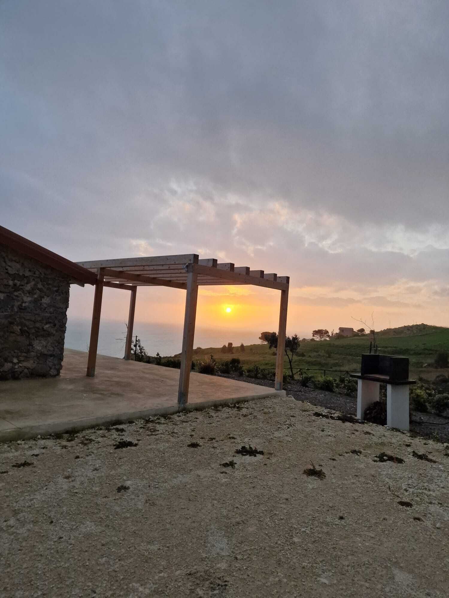 A covered outdoor area with a stone building, a gravel ground, and a sunset in the background.