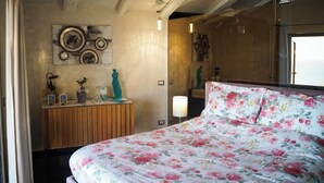 A bedroom with a floral bedspread, a wooden dresser with decorative items, and a wall-mounted mirror.