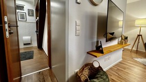 A modern living room with a wooden floor, a mounted TV, a wooden shelf, a lamp, and a basket. - Modern apartment with charm (Kehl)