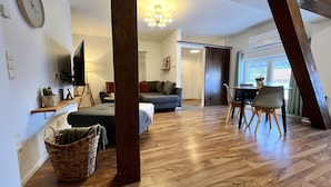 A spacious living area with a wooden floor, a sofa, a dining table with chairs, a television, and a chandelier. - Modern apartment with charm (Kehl)