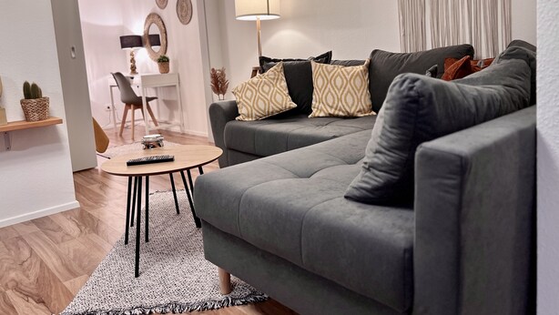 A modern living room with a grey sofa, a round coffee table, and a lamp. There is a dining area in the background with a white table and chairs. - Modern apartment with charm (Kehl)