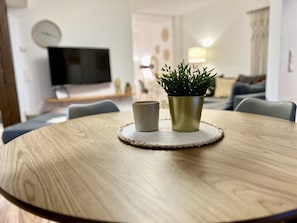 Une table ronde en bois, surmontée d’un set de table en fibres tressées, une tasse grise et une plante verte dans un pot doré.