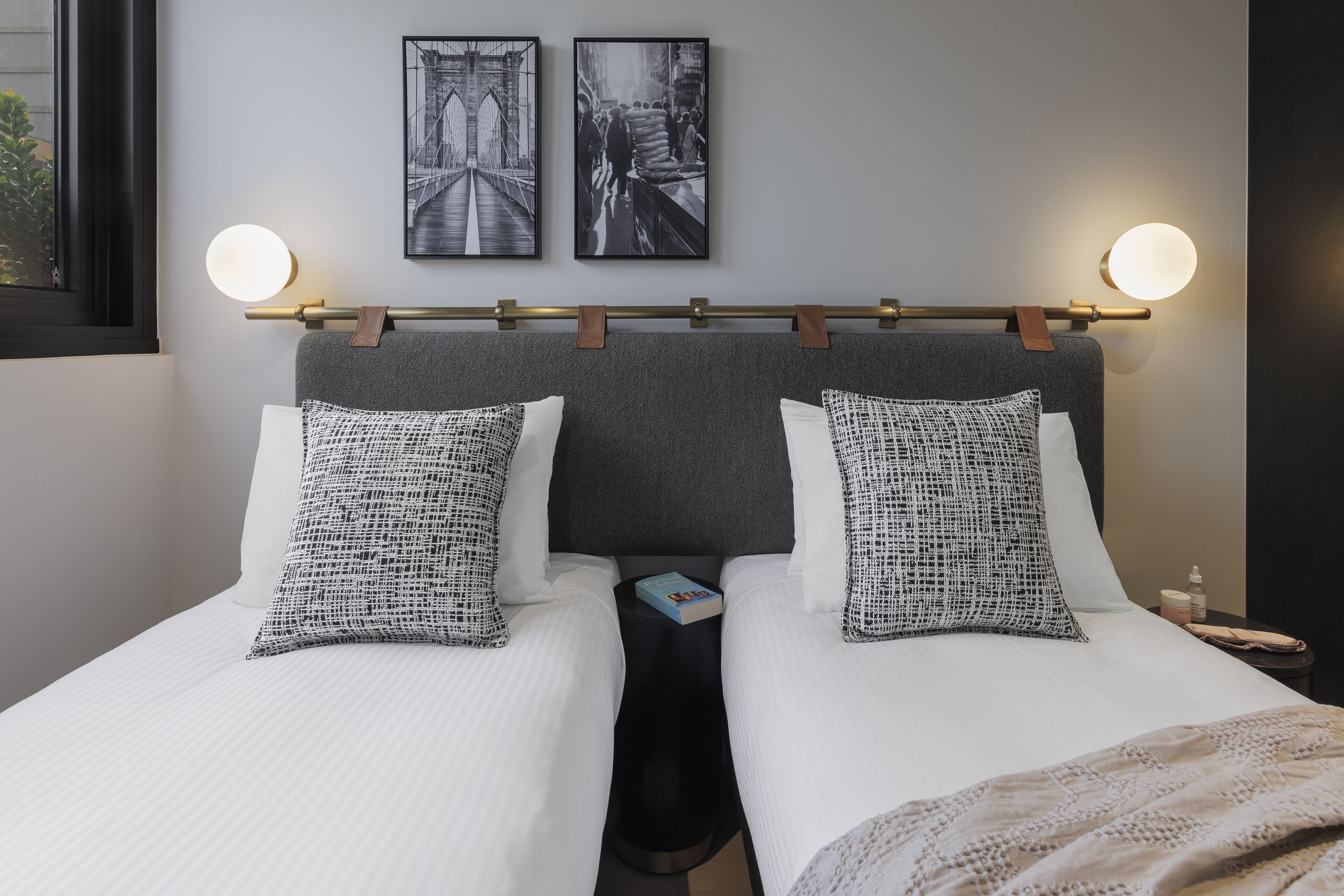 Et hotelværelse med en dobbeltseng, to puder, et natbord med en bog og to vægmonterede lamper.