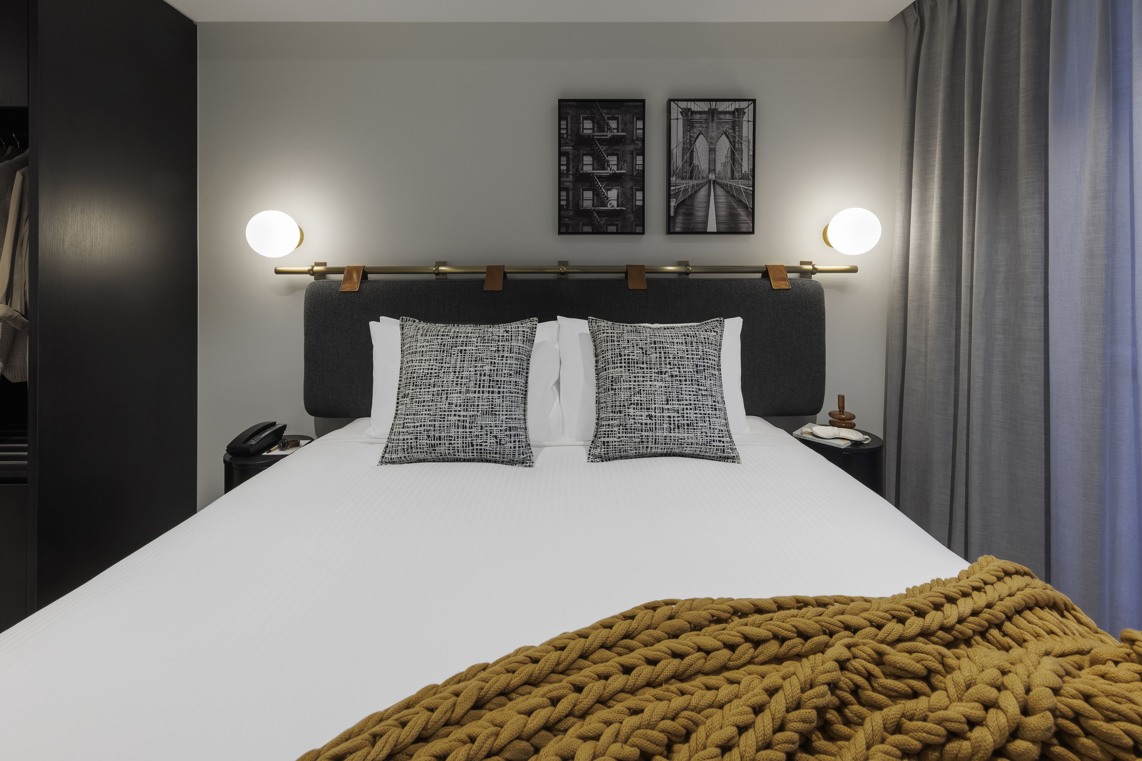 Habitación de hotel con una cama grande, dos almohadas, una mesita de noche con lámpara, teléfono y una lámpara de pared.