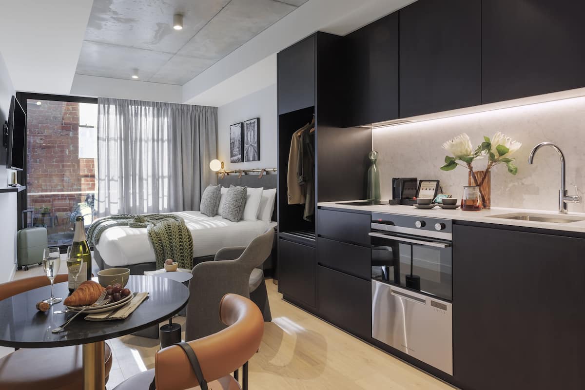 Una habitación de hotel moderna con kitchenette, zona de comedor y cama con vistas a la ciudad.