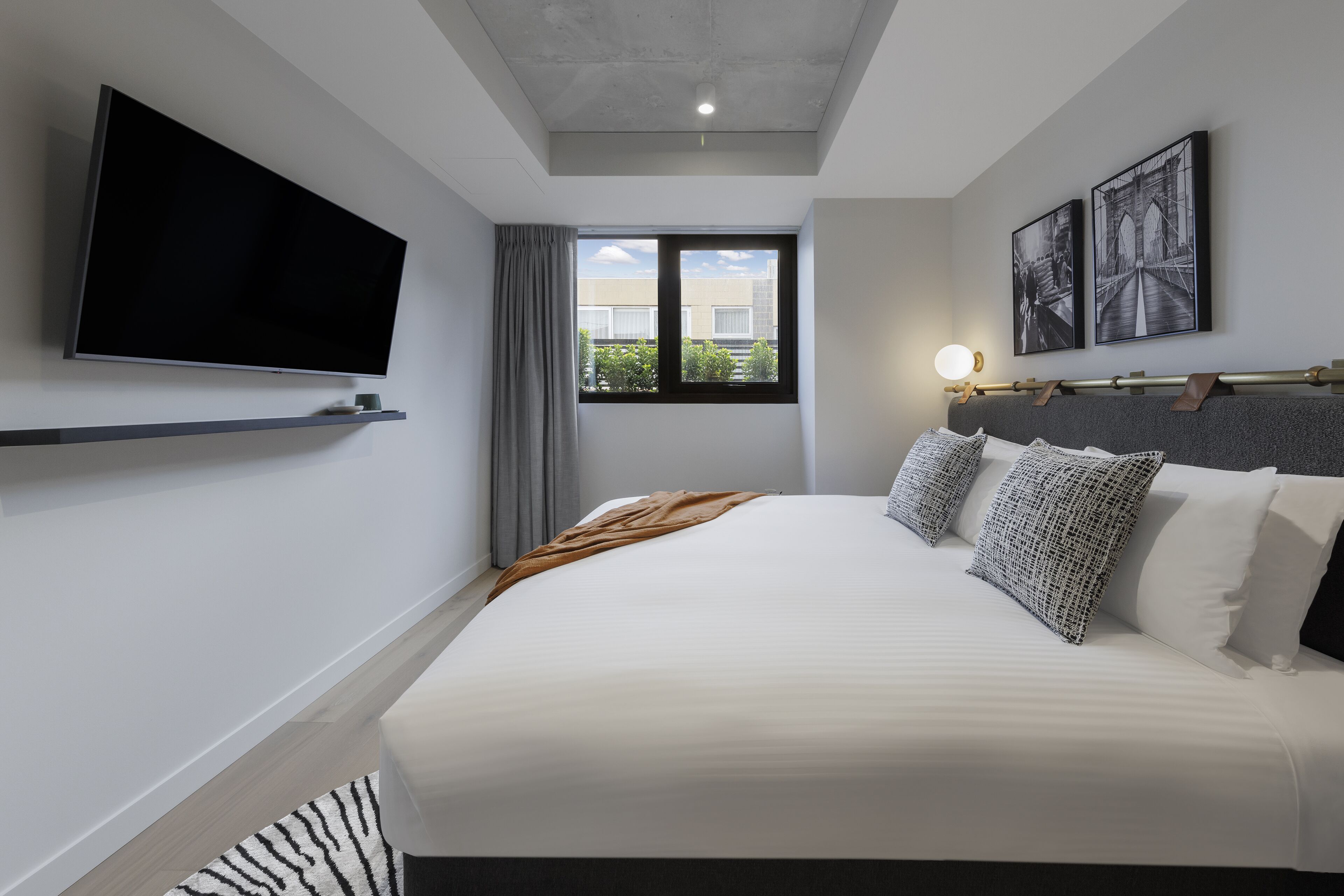 Ein modernes Hotelzimmer mit einem großen Bett, einem Flachbildfernseher, einem Fenster mit Blick ins Grüne und zwei gerahmten Bildern an der Wand.