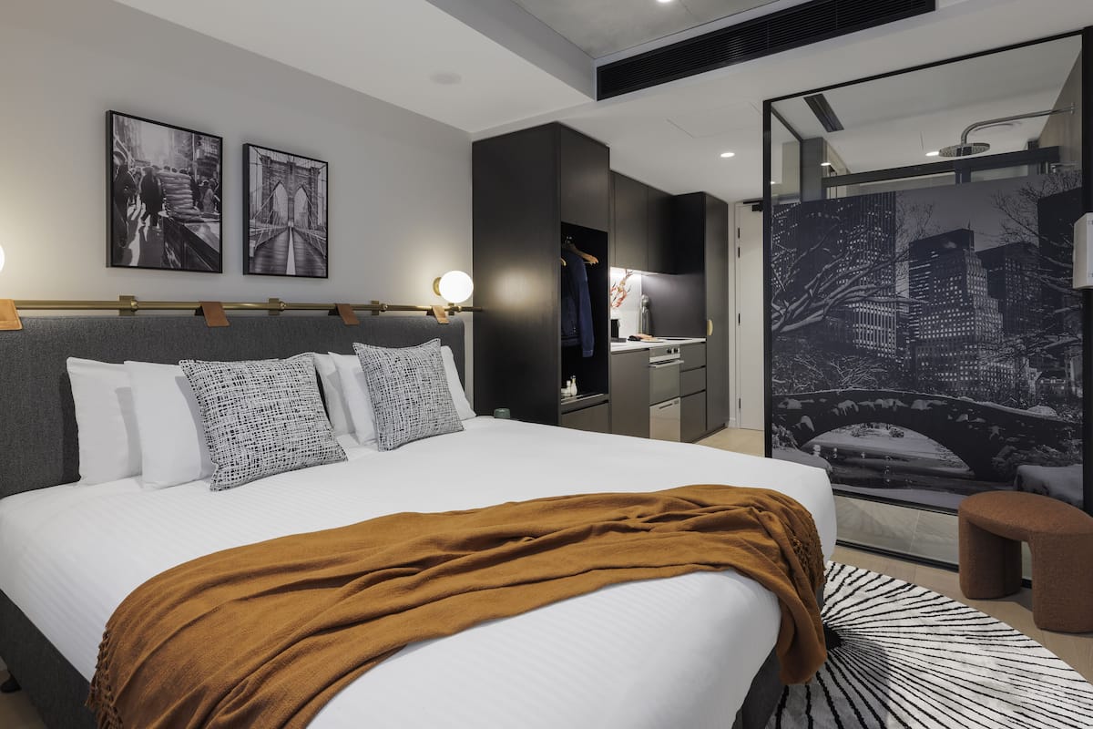 Un dormitorio moderno con una cama grande, un escritorio y vistas a un paisaje urbano a través de un ventanal.