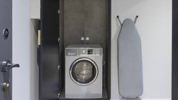 Ein kompakter, moderner Waschraum mit integrierter Waschmaschine und Trockner, einem kleinen Bügelbrett und einer Tür mit Schlüsselsperre.
