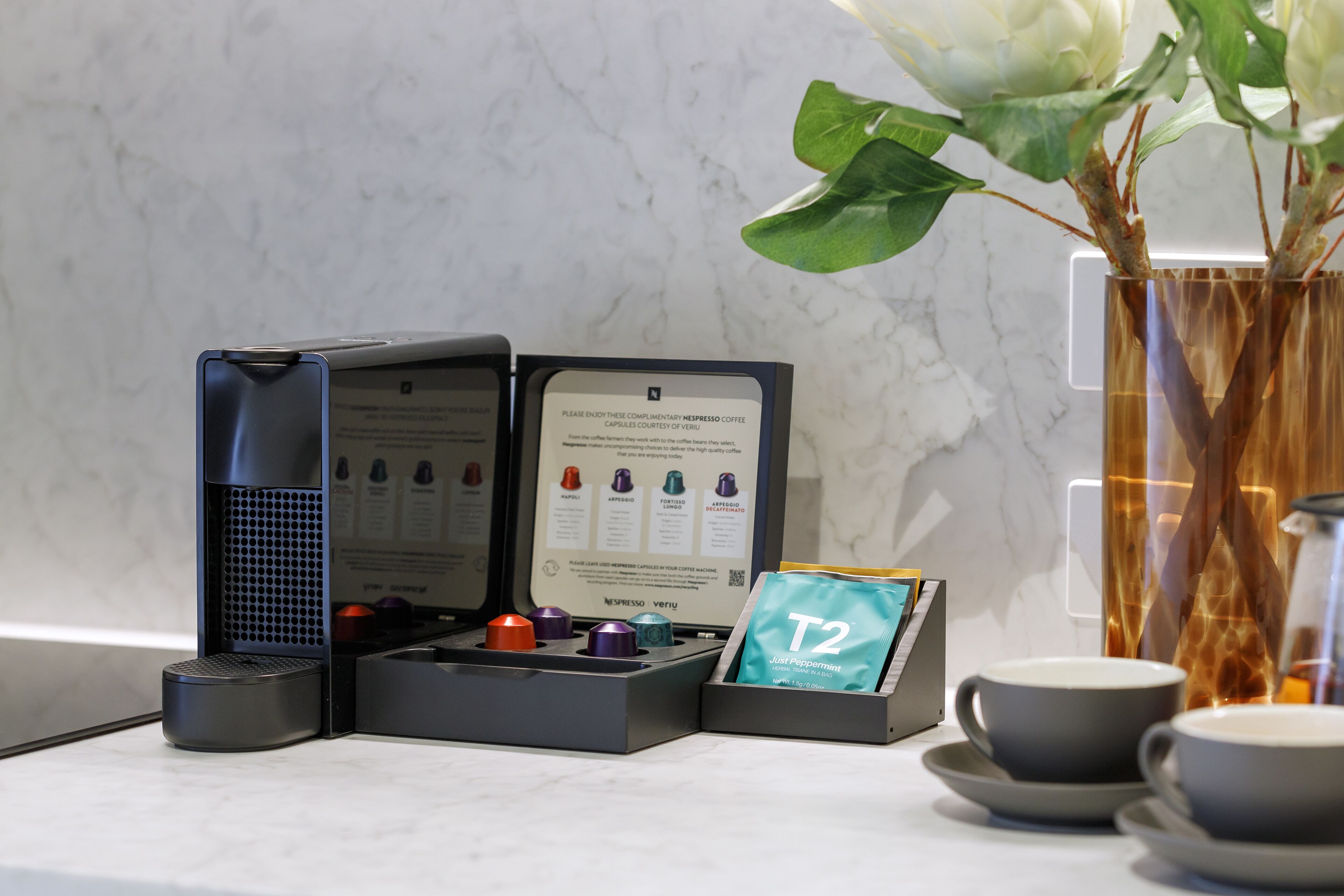 Eine Kapselkaffeemaschine, eine Karte und zwei Tassen auf einer Marmorarbeitsplatte.