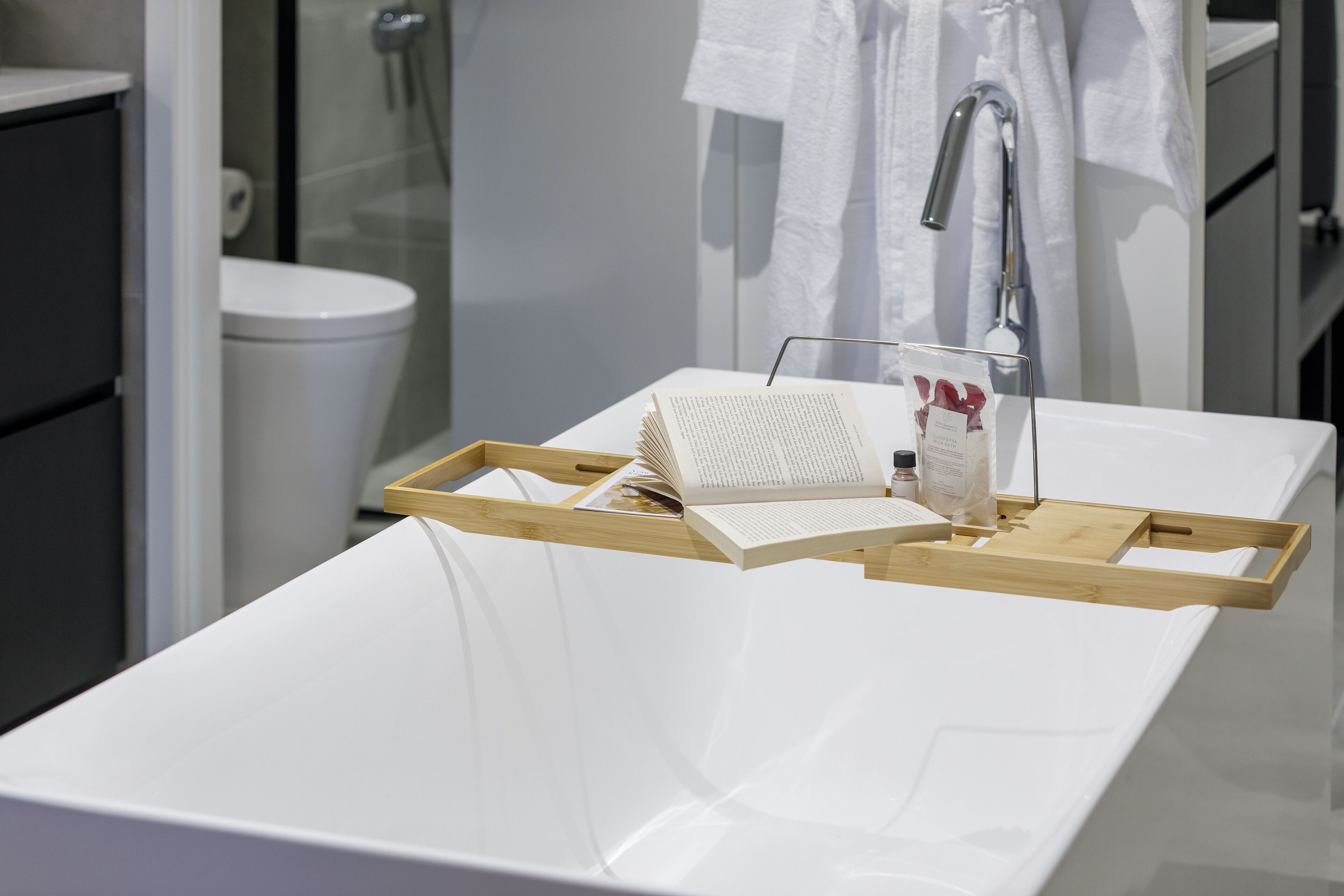 A modern bathroom with a white bathtub, a wooden tray, and a book.