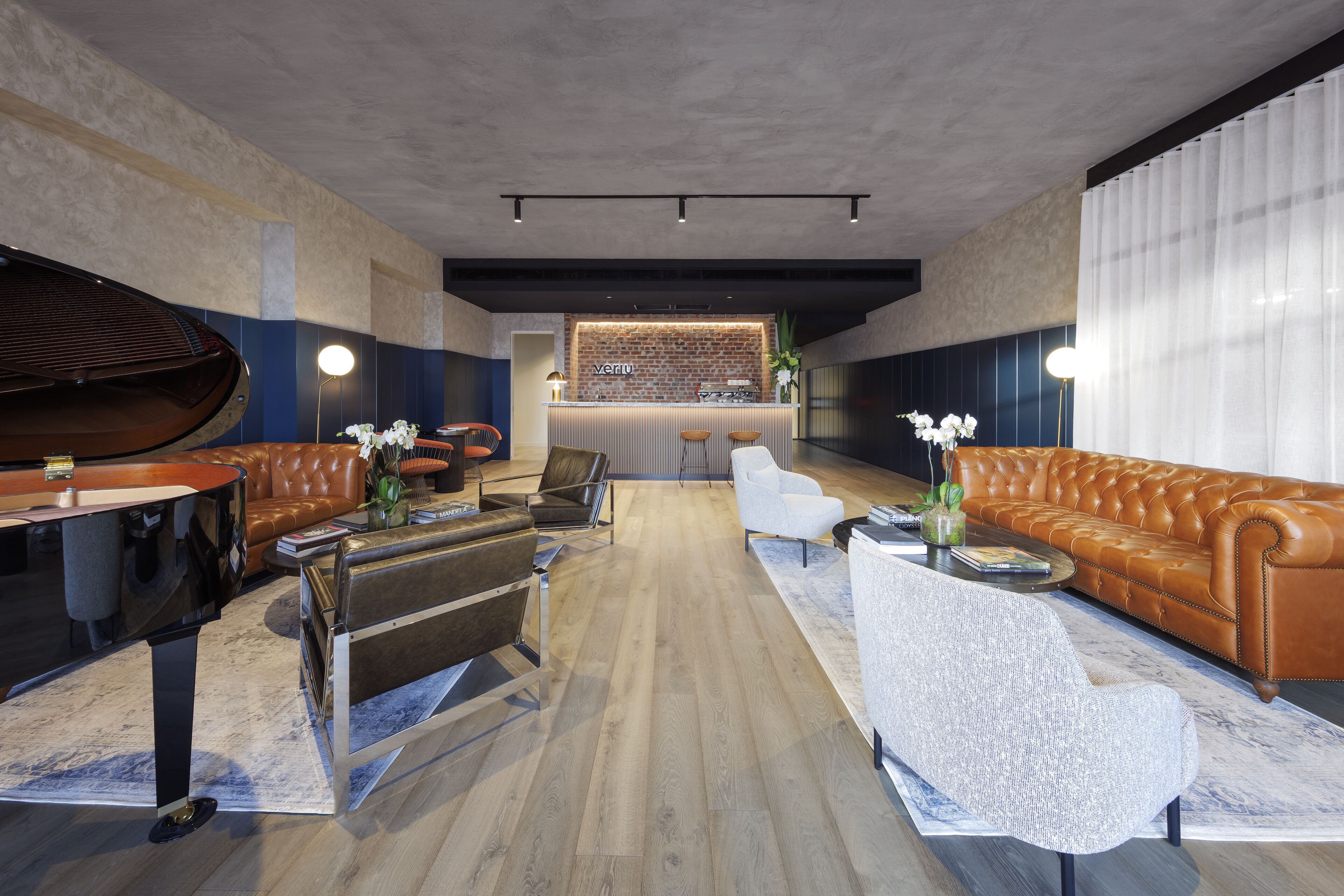 A modern lounge area with a piano, leather sofas, a bar, and a wooden floor.