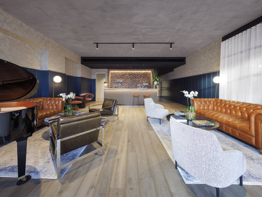 Un área lounge moderna con un piano, sofás de cuero, un bar y piso de madera.