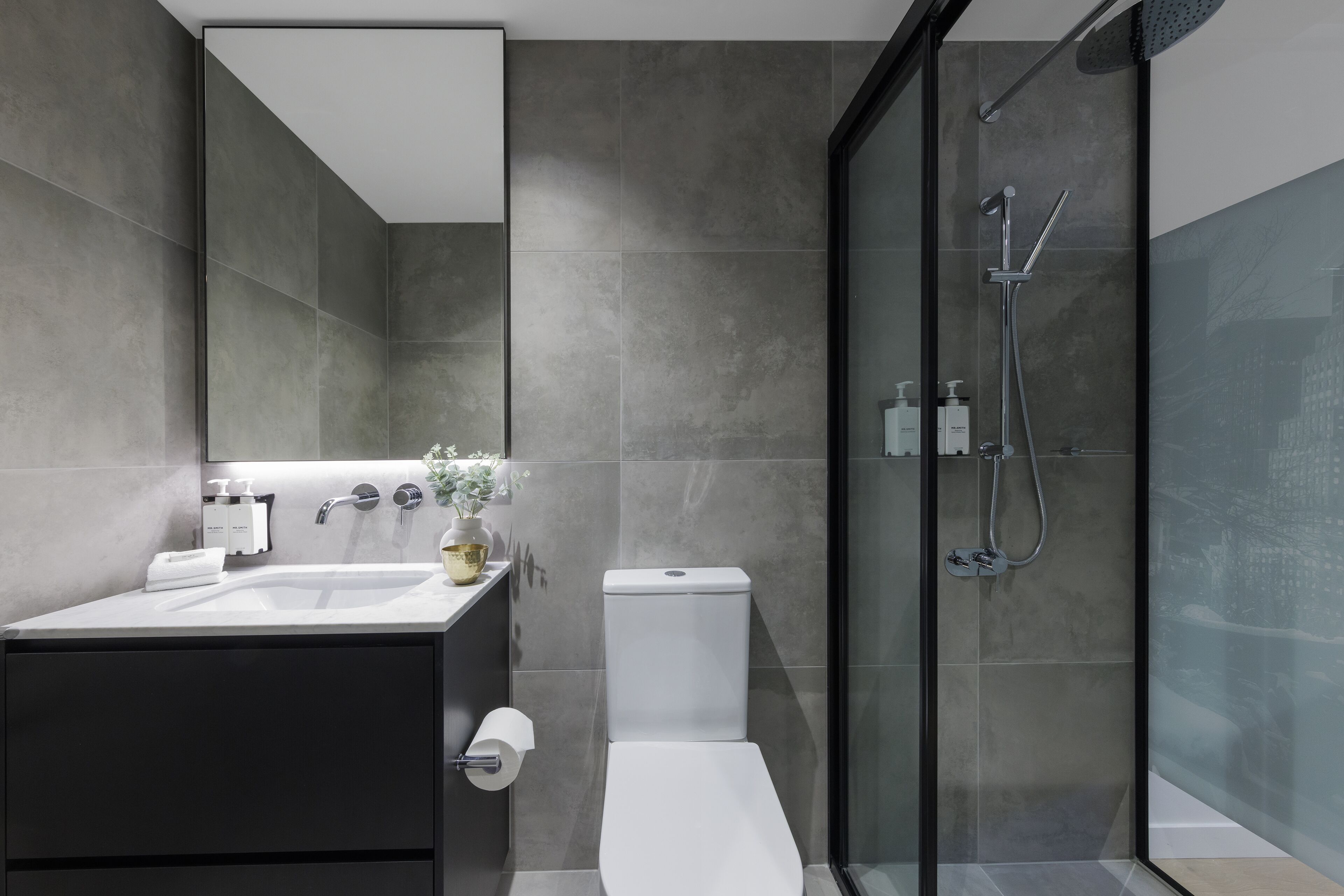 Un bagno moderno con doccia vetrata, un water bianco e un mobile lavabo scuro con lavandino e specchio.