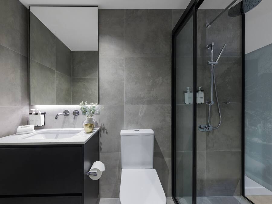 Un bagno moderno con doccia vetrata, un water bianco e un mobile lavabo scuro con lavandino e specchio.