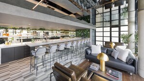 Een moderne bar met een lange toonbank, barstoelen en een zithoek met een bank en fauteuils.