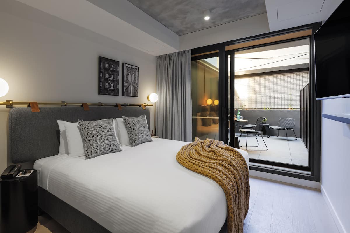 Habitación de hotel moderna con una cama grande, vistas al patio exterior y una puerta corrediza de vidrio.