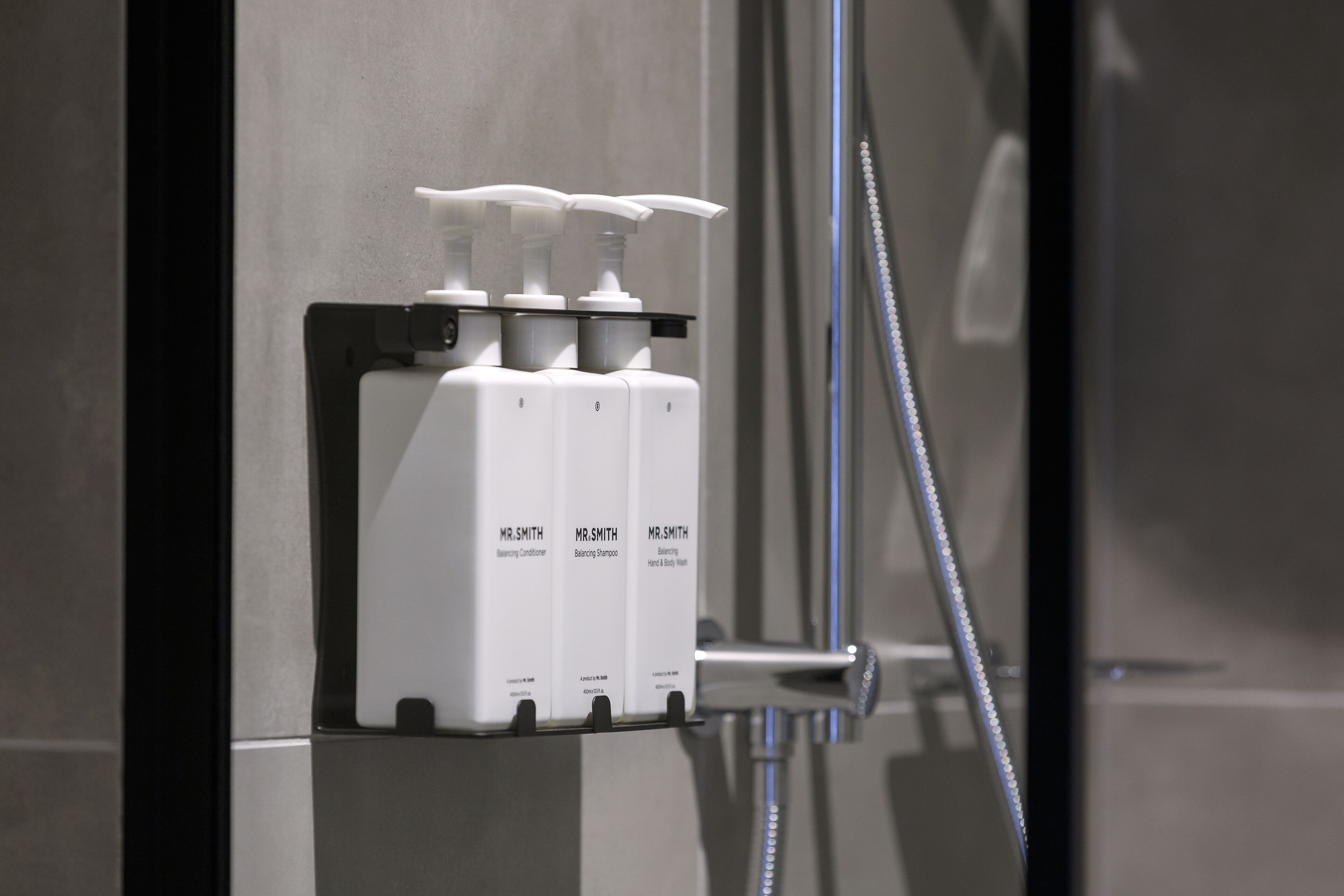 A bathroom with three Mr. Smith shampoo bottles on a wall-mounted dispenser.