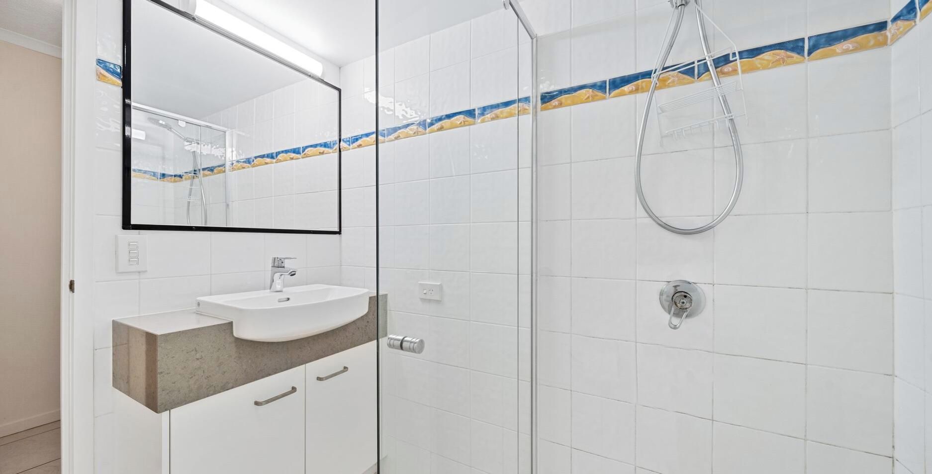 A bathroom with a white sink, a mirror, and a shower with a glass door.