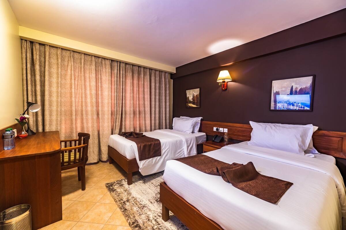 A hotel room with two beds, a desk, a chair, a lamp, and a picture on the wall.