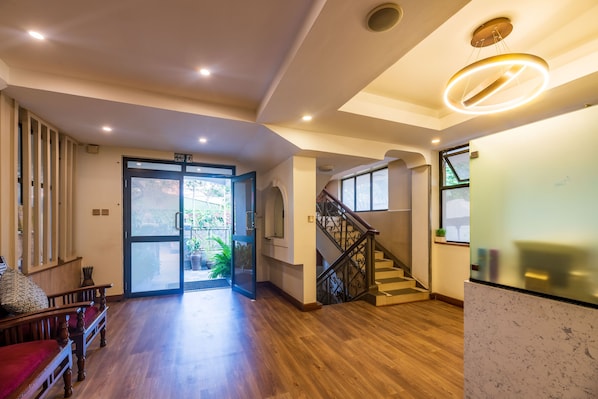 A spacious lobby with a wooden floor, a staircase, and a glass door leading outside. - Samra Hotel (Nairobi)