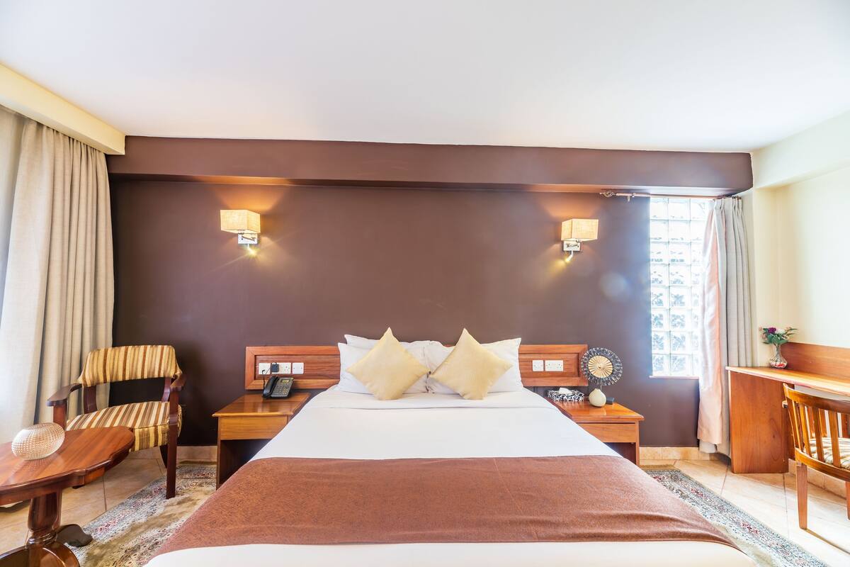 A hotel room with a large bed, two bedside tables, a chair, a desk, and a window with curtains.