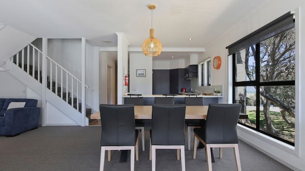 A modern kitchen with a central island, a dining area with a wooden table and black chairs, and a staircase leading to another level.