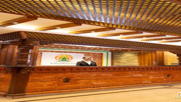 A wooden reception desk with a logo and a person standing behind it. - MeroStay 001 Hotel Kailash Kutee (Kathmandu)