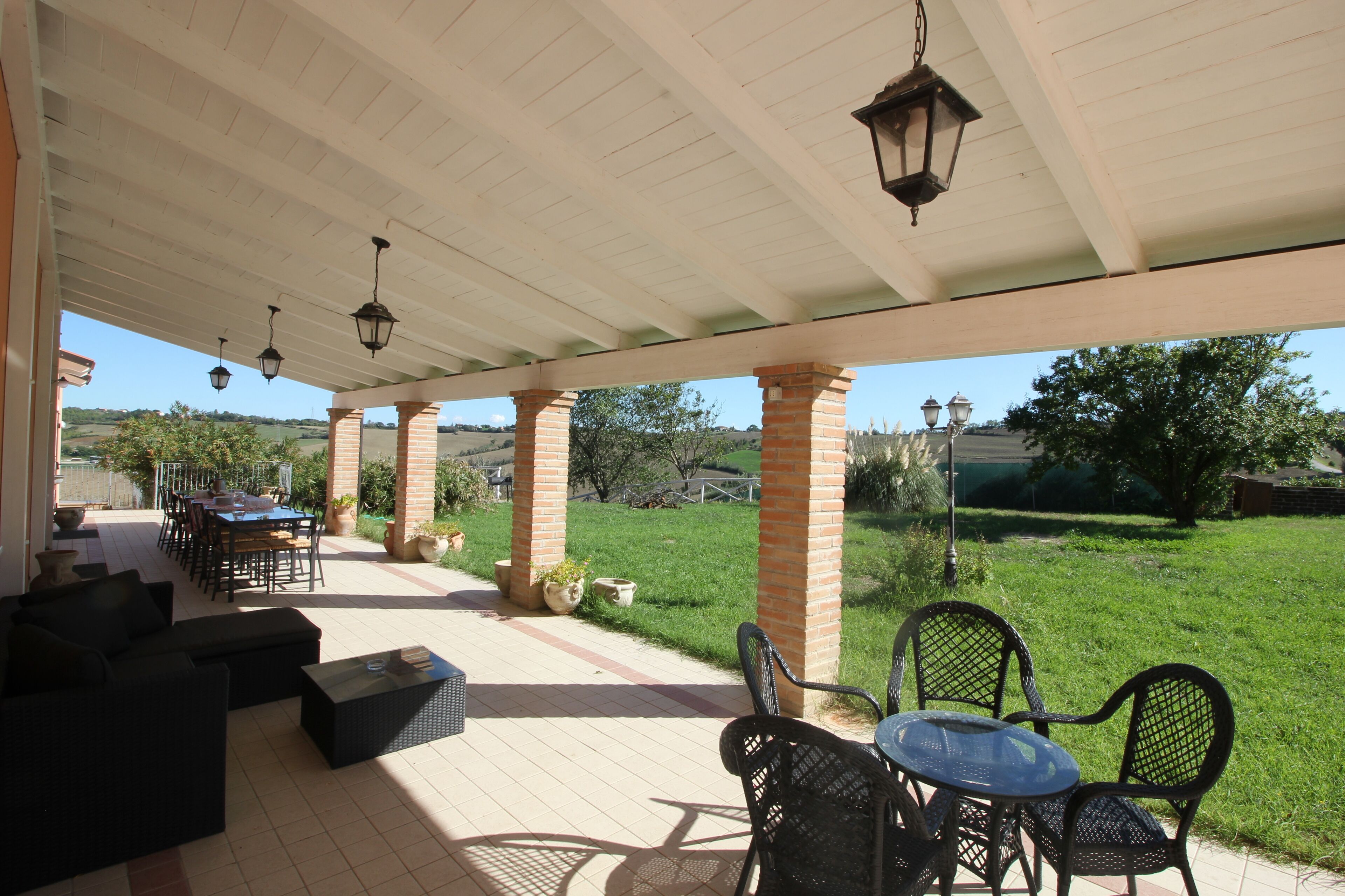 Un patio cubierto con muebles de exterior, una mesa y faroles colgantes.