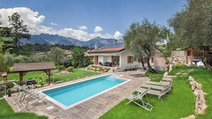 Ein Poolbereich mit Liegestühlen, einer Pergola und einer Steindeckterrasse.