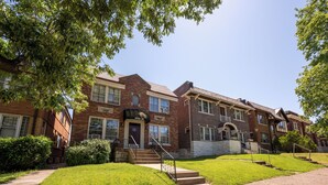 A row of brick townhouses with a central entrance, steps, and a small lawn area. - One-bedroom-City Livin' (Saint Louis)