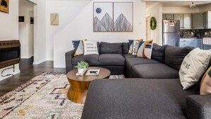 Un salon moderne avec un canapé d’angle, une table basse ronde et un grand tableau accroché au mur.