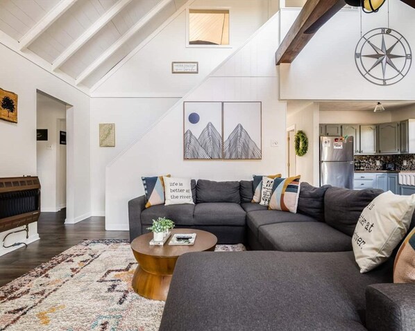 Un salon moderne avec un canapé d’angle, une table basse ronde et un grand tableau accroché au mur.